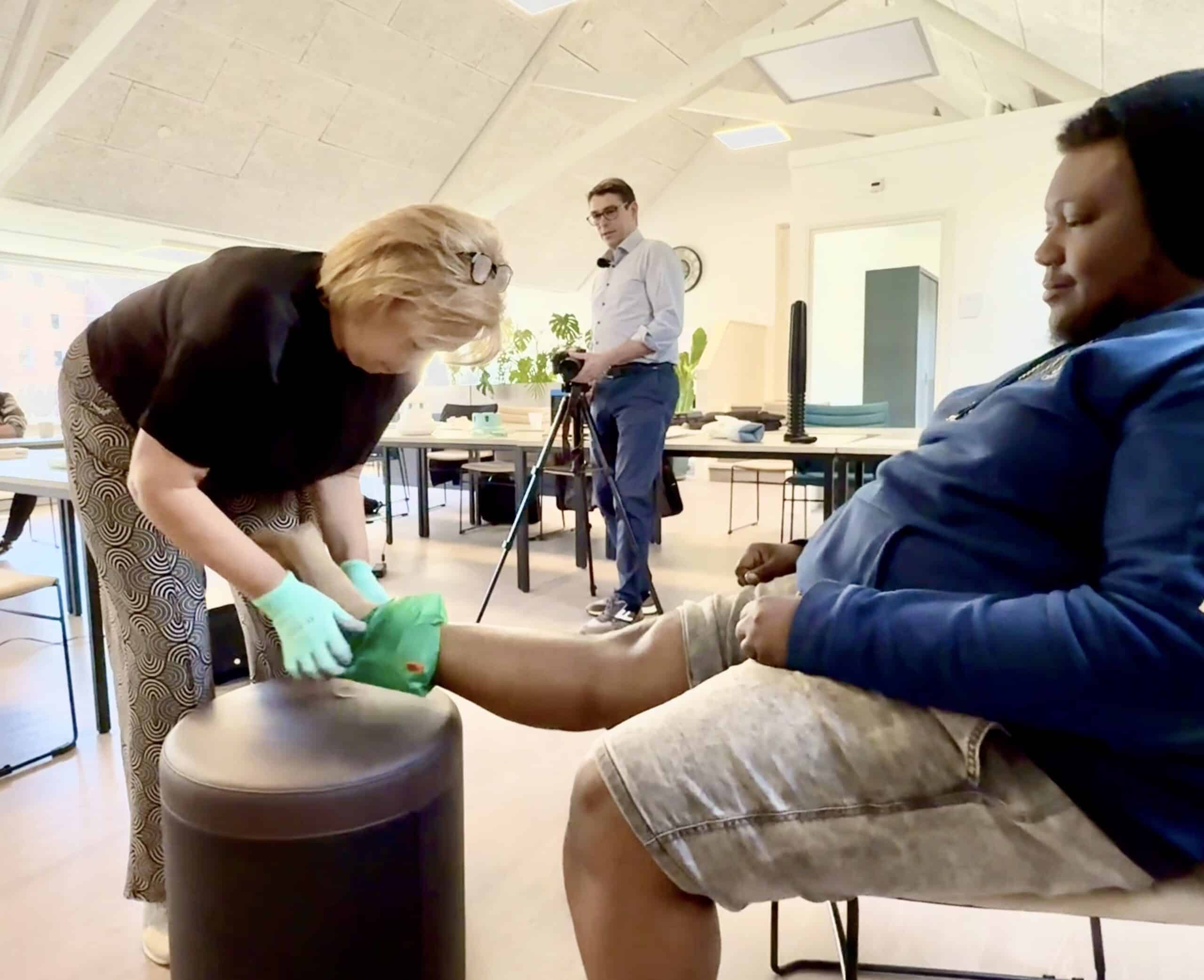 Verzorgende trekt bij client steunkous aan tijdens ergonomisch onderzoek, met glijzak